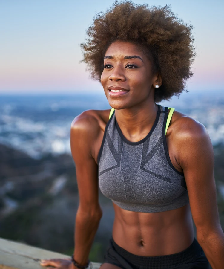 Confident athletic woman in workout clothes posing on urban rooftop at golden hour sunset