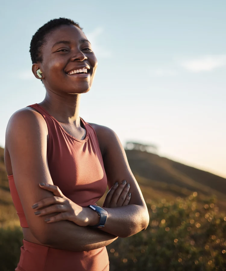 Confident woman in athletic wear smiling outdoors during golden hour fitness wellness moment