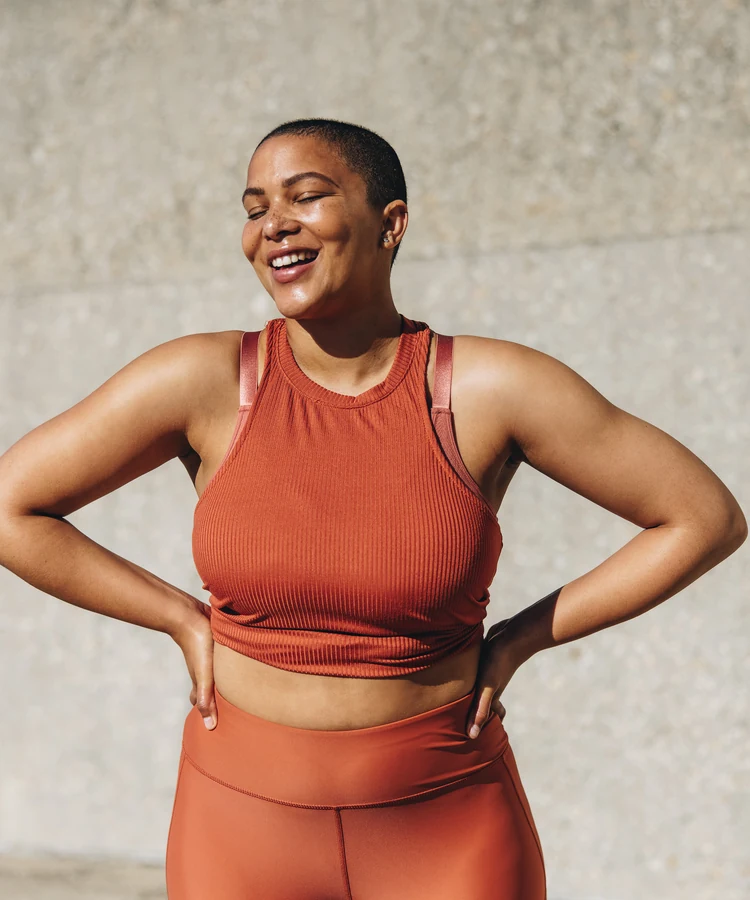 Confident woman in orange athletic wear poses with hands on hips showing body positivity and fitness wellness