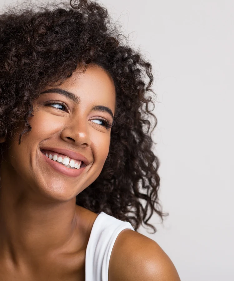 Happy woman with curly hair smiling confidently in white tank top promoting wellness and self-care