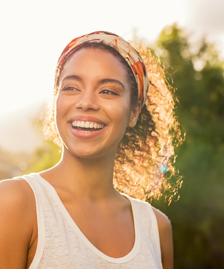 Happy woman with curly hair smiling outdoors in golden sunlight representing wellness and joy