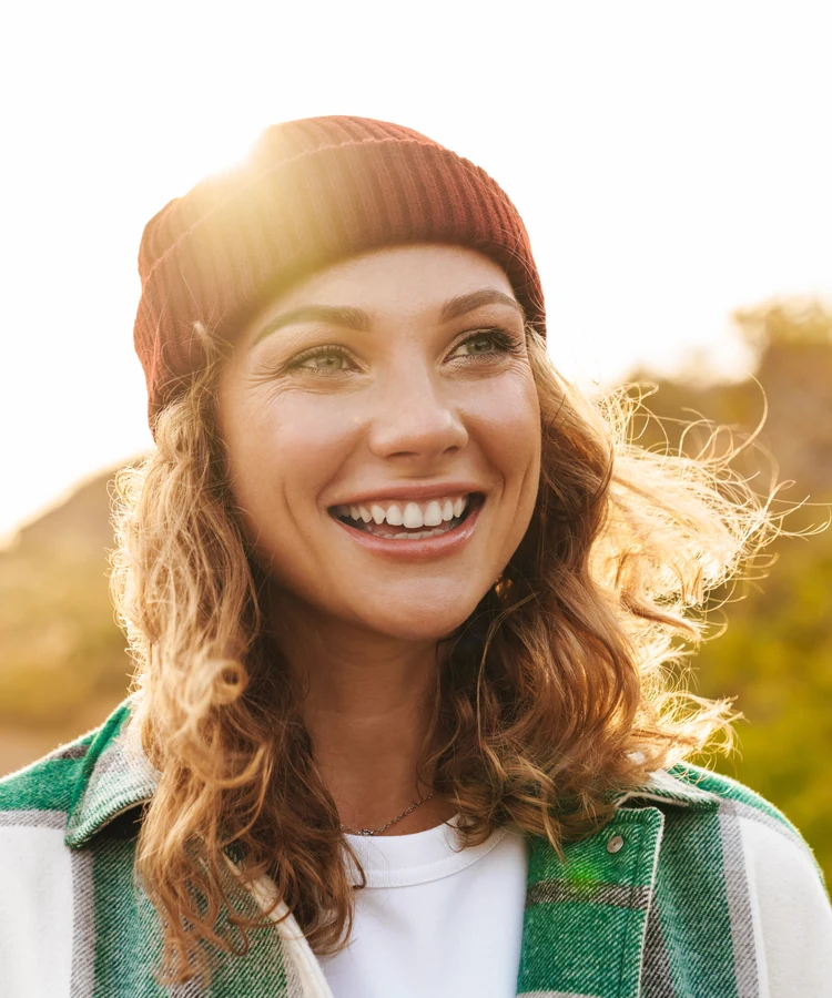 Happy woman wearing beanie and flannel shirt smiling outdoors in golden sunlight for wellness lifestyle