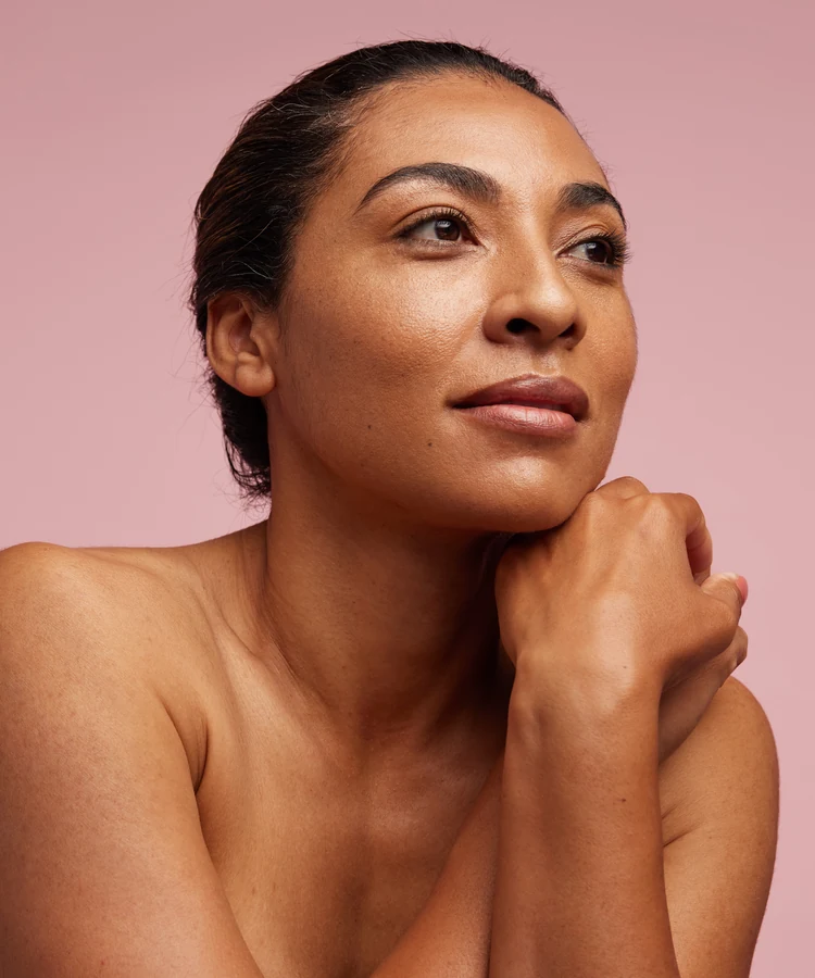 Confident woman with natural makeup and slicked back hair in beauty wellness portrait against pink background