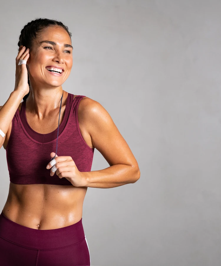 Smiling fit woman in burgundy activewear exercising with earbuds showing healthy lifestyle and fitness goals