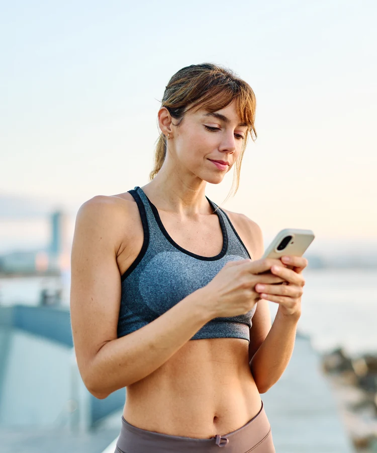 Confident woman in athletic wear checking smartphone after outdoor workout in urban setting
