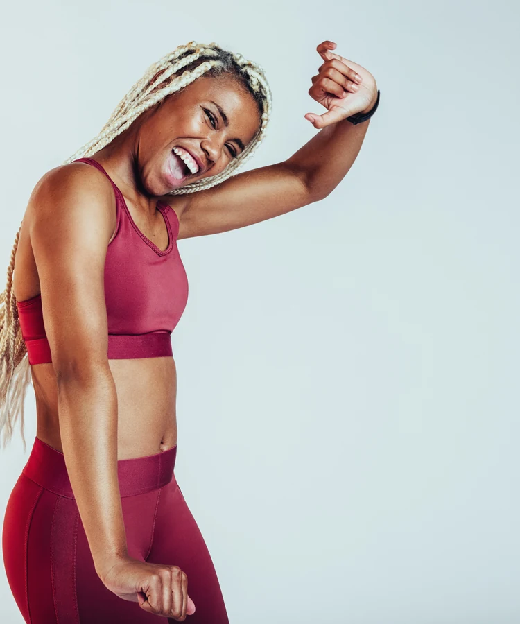 Confident woman in burgundy athletic wear flexing bicep showing fitness strength results