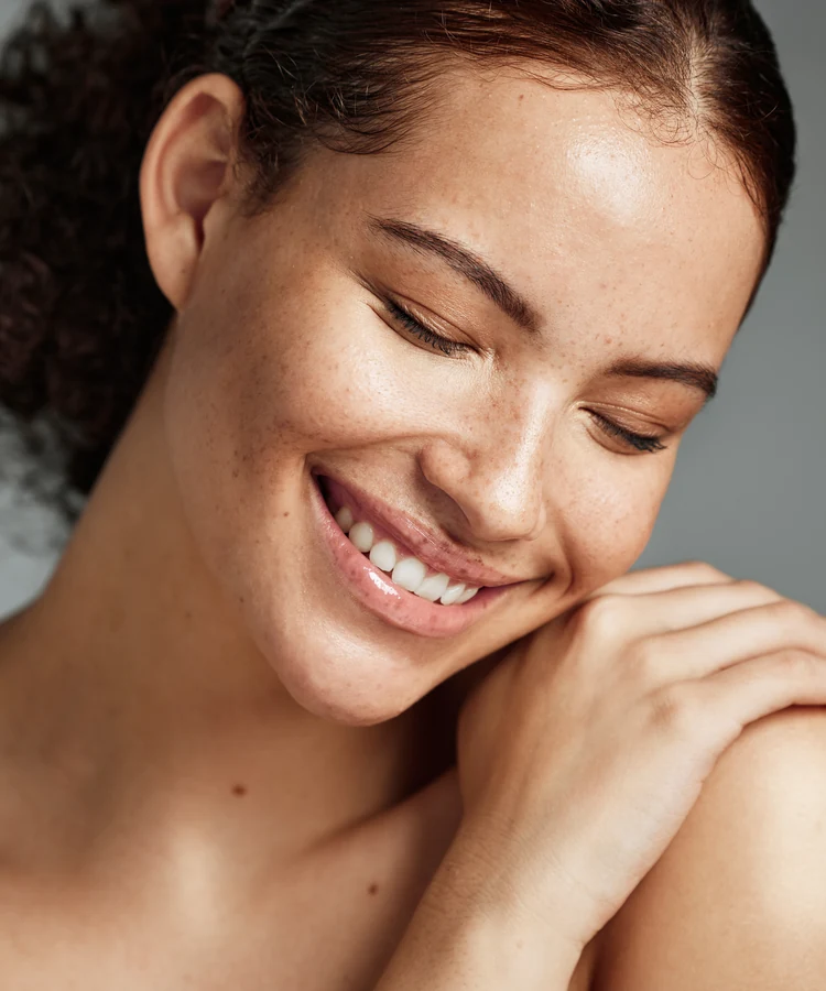 Beautiful woman with glowing skin touching shoulder and smiling confidently in wellness portrait