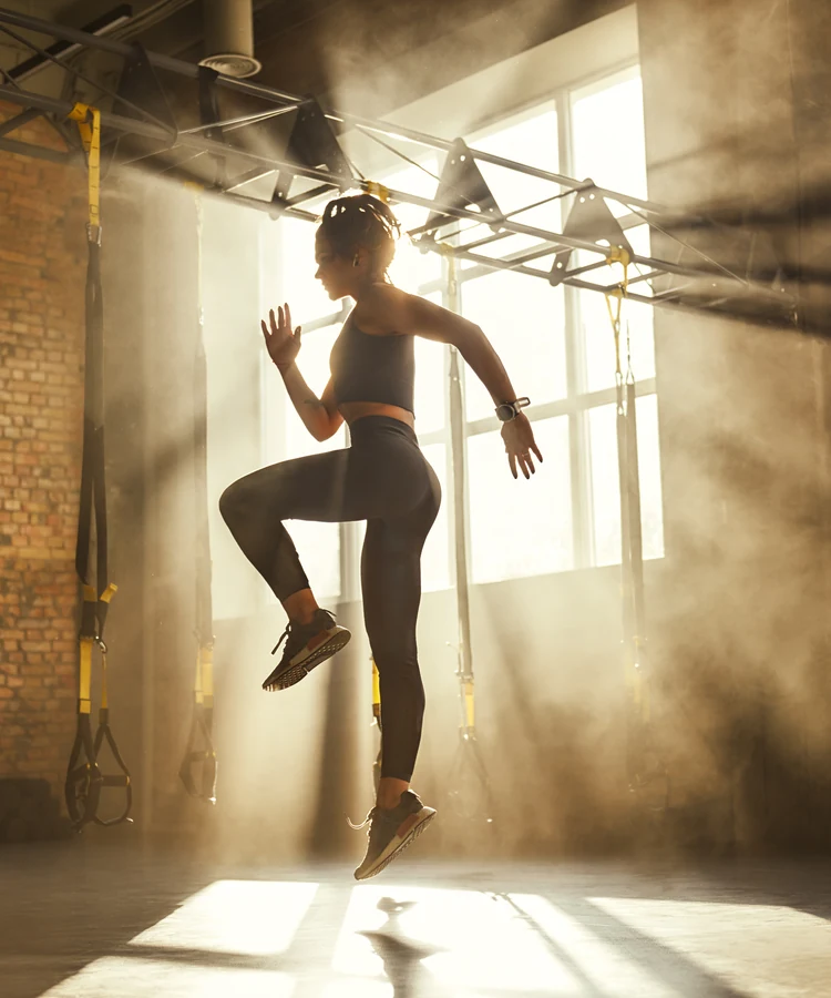 Energetic woman performing high knee cardio exercises in bright gym for weight loss fitness routine