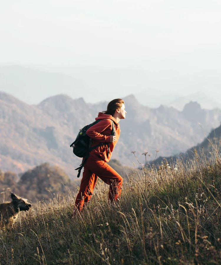 Determined woman hiking uphill mountain trail in orange athletic wear carrying backpack for fitness and weight loss