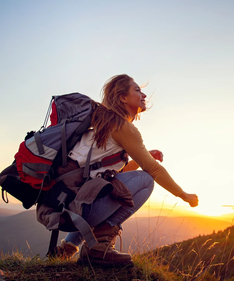 Woman with backpack hiking on mountain ridge at sunset, outdoor fitness and wellness adventure