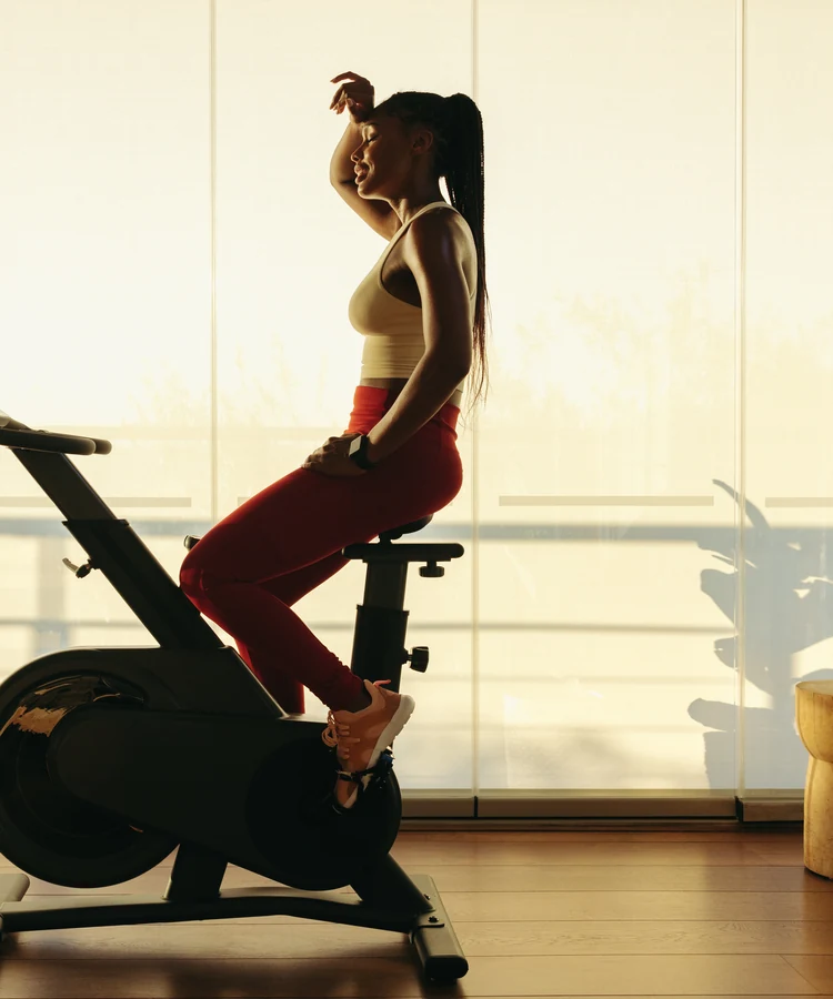 Woman exercising on stationary bike at home in modern living room with natural lighting for fitness wellness