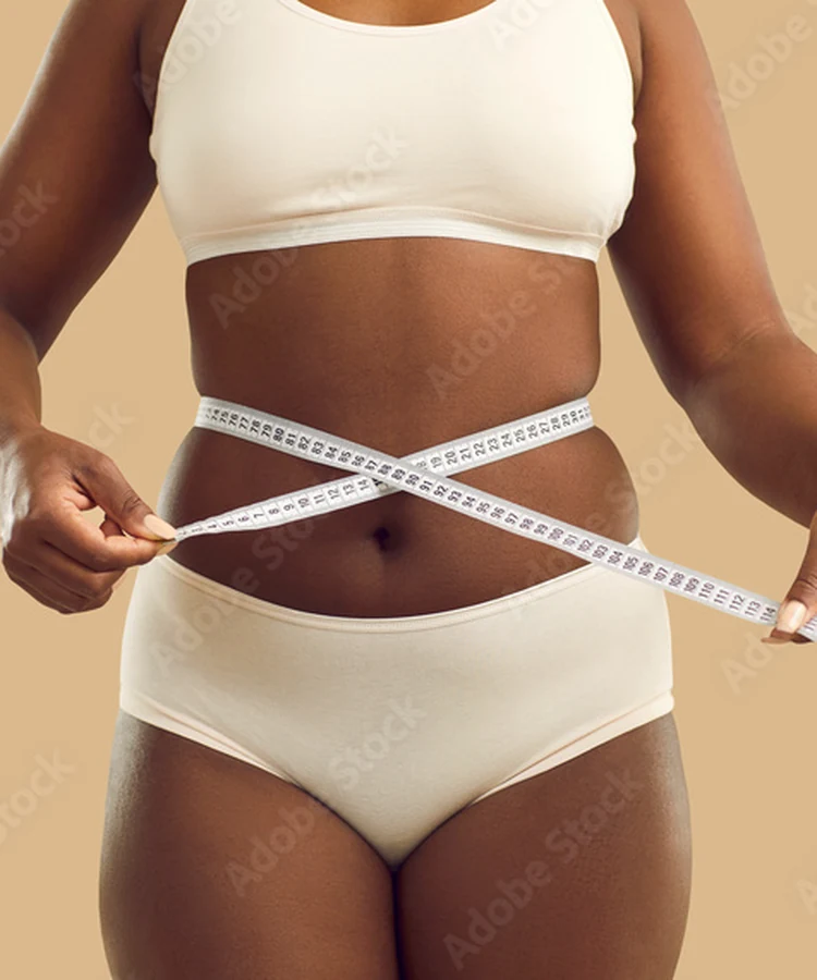 Woman in white athletic wear measuring her waist with measuring tape for weight loss progress tracking
