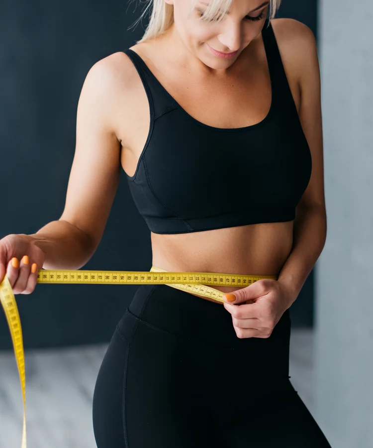 Woman in black athletic wear measuring waist with yellow measuring tape for fitness tracking