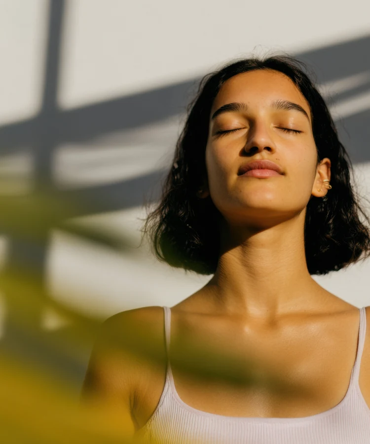 Woman practicing mindful meditation in golden sunlight for wellness and mental health benefits