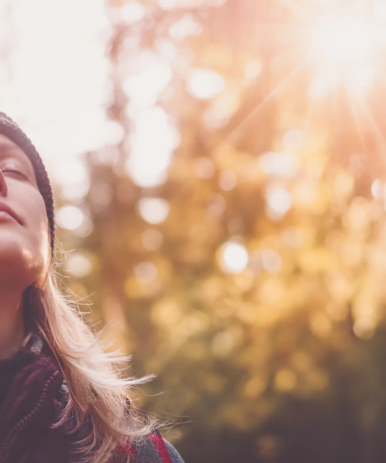Woman practicing mindful breathing outdoors in golden sunlight for wellness and stress relief