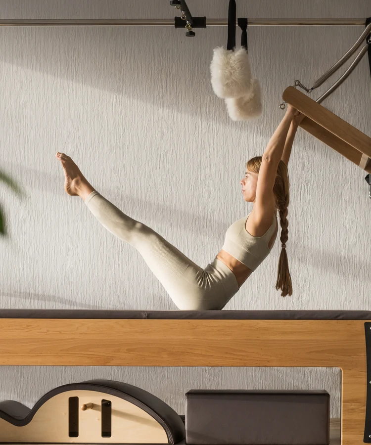 Woman performing pilates exercise on wooden reformer machine in bright studio for wellness and fitness