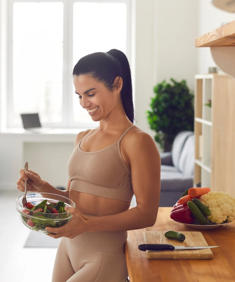 Woman in athletic wear preparing healthy salad in bright modern kitchen for weight loss wellness