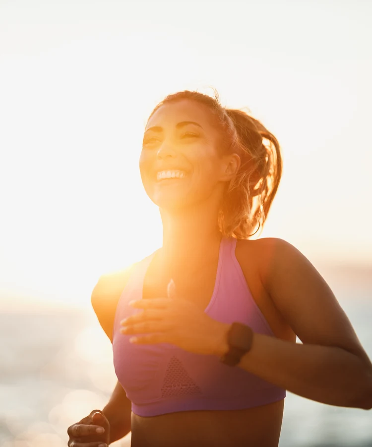Happy woman jogging outdoors in pink athletic wear during golden hour sunset workout