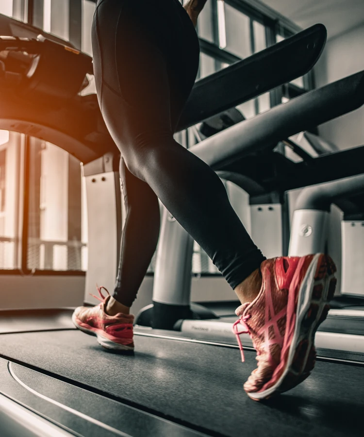 Woman exercising on treadmill in modern gym wearing athletic wear and pink running shoes