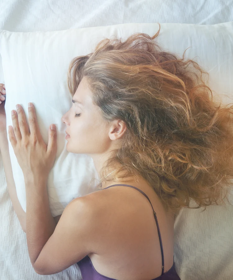 Woman with curly hair sleeping peacefully on white bedding for wellness and rest health