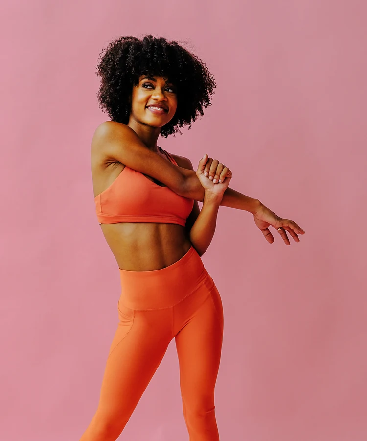 Confident woman with curly hair stretching in orange athletic wear during fitness routine