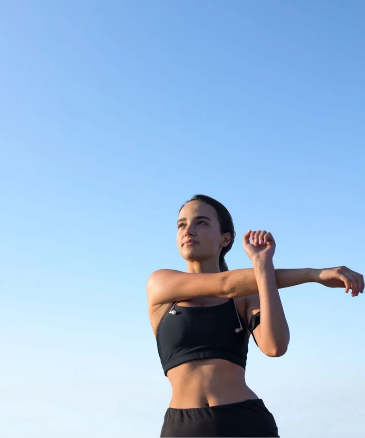 Woman stretching arms during outdoor fitness routine against clear blue sky for wellness and health