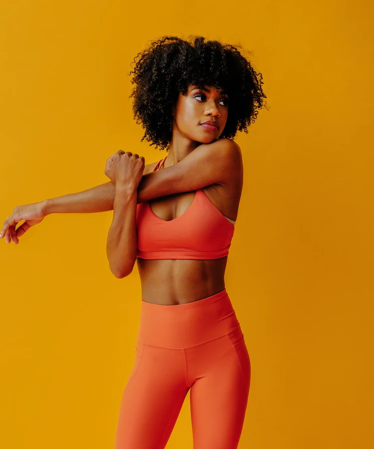 Confident woman in coral fitness wear performing arm stretch exercise for wellness and flexibility
