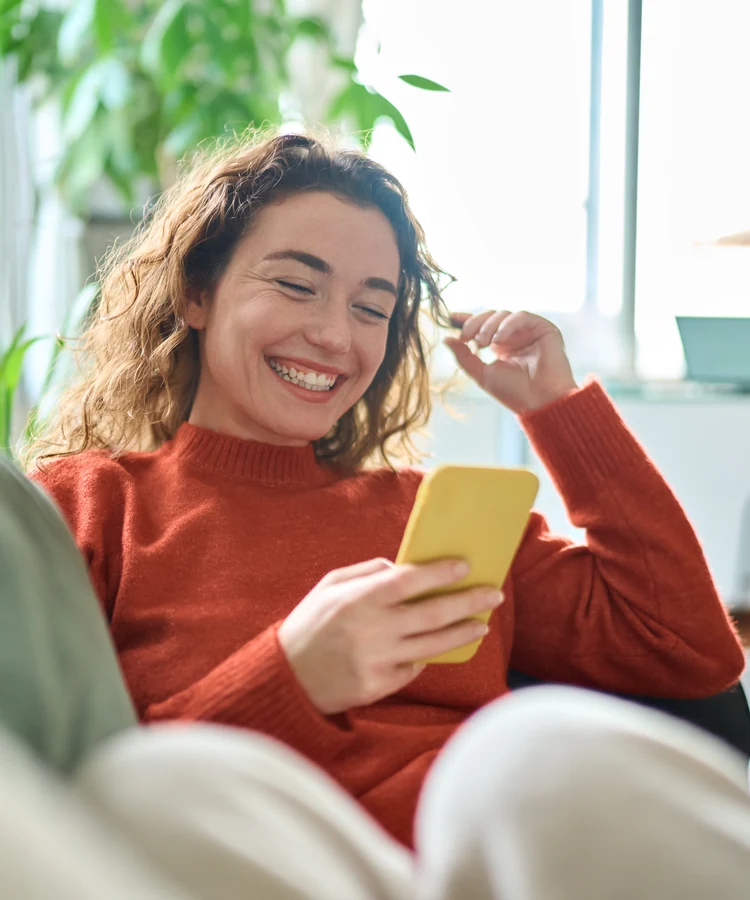 Happy woman with braces using smartphone while relaxing comfortably at home for telehealth consultation
