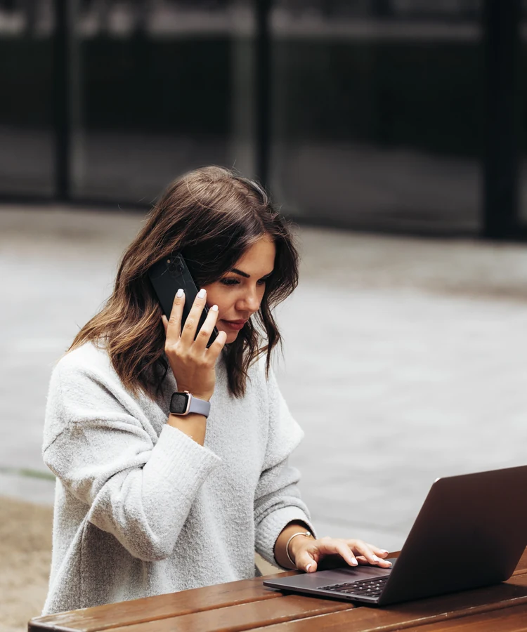 Professional woman managing wellness consultation call while working on laptop outdoors at wooden table