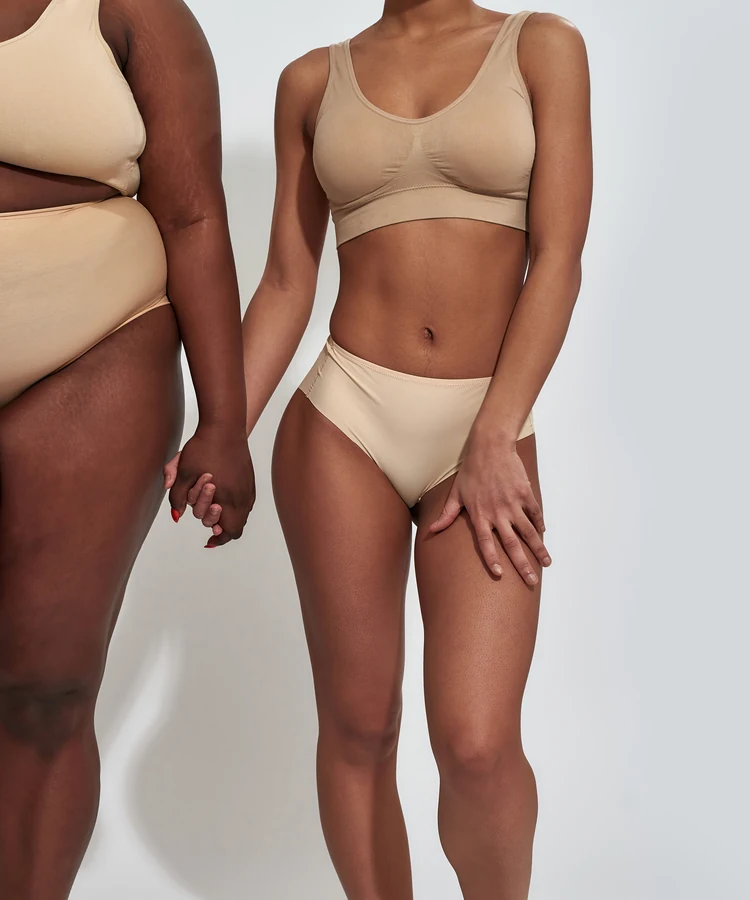 Two women of different body types holding hands in beige underwear showing body positivity and self-acceptance