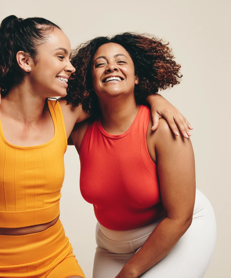 Three happy women in colorful athletic wear laughing and embracing together showing wellness and friendship